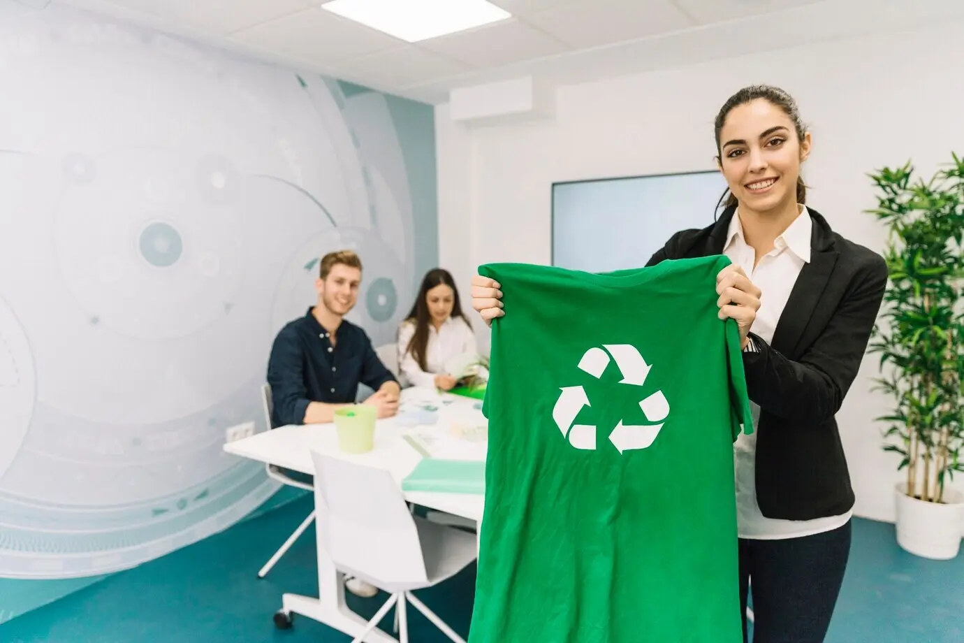 Porträt einer glücklichen jungen Geschäftsfrau, die ein grünes T-Shirt mit Recycling-Symbol zeigt.