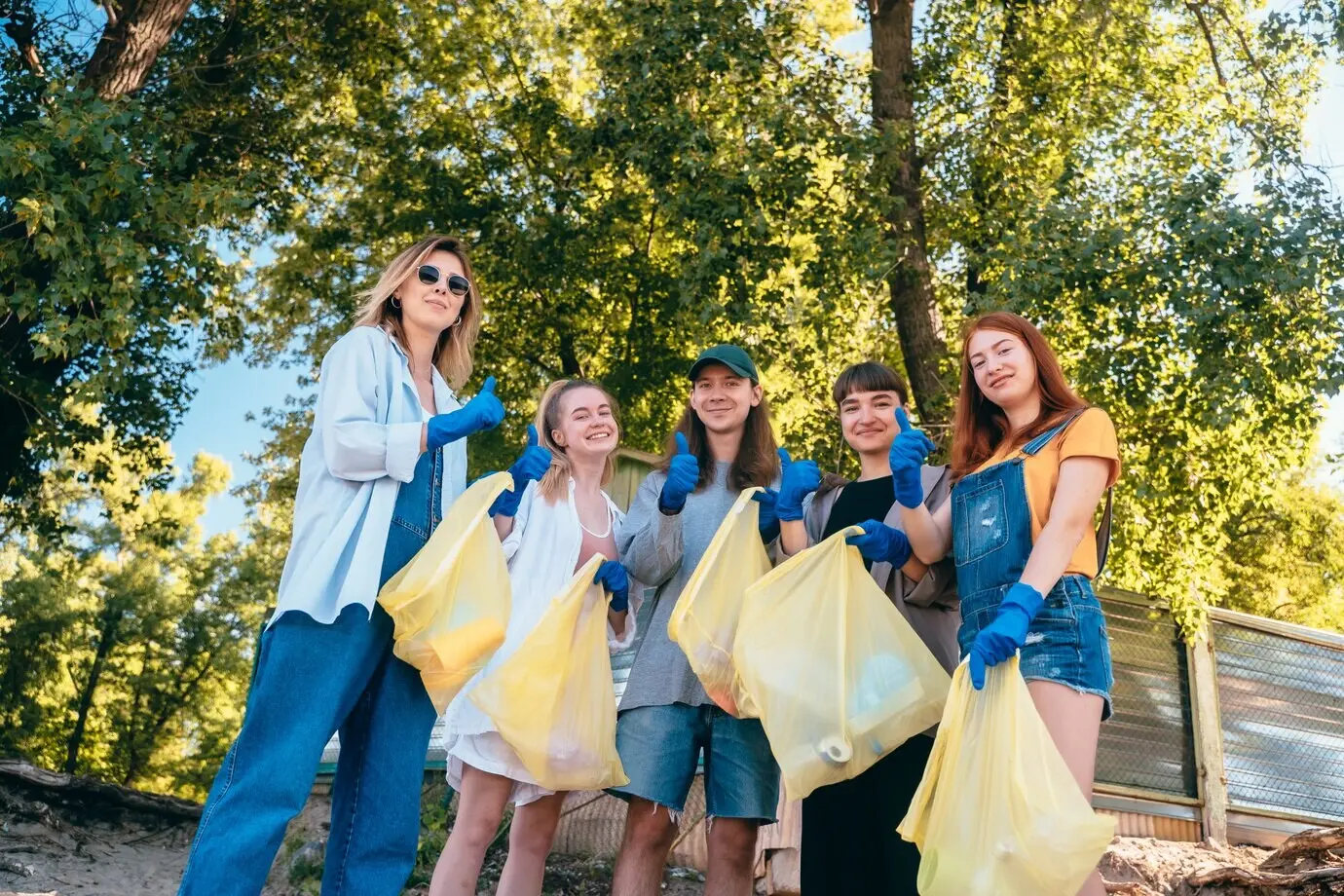 Eine Gruppe befreundeter Aktivisten sammelt Plastikmüll am Strand. Die Jungs zeigen Daumen hoch.