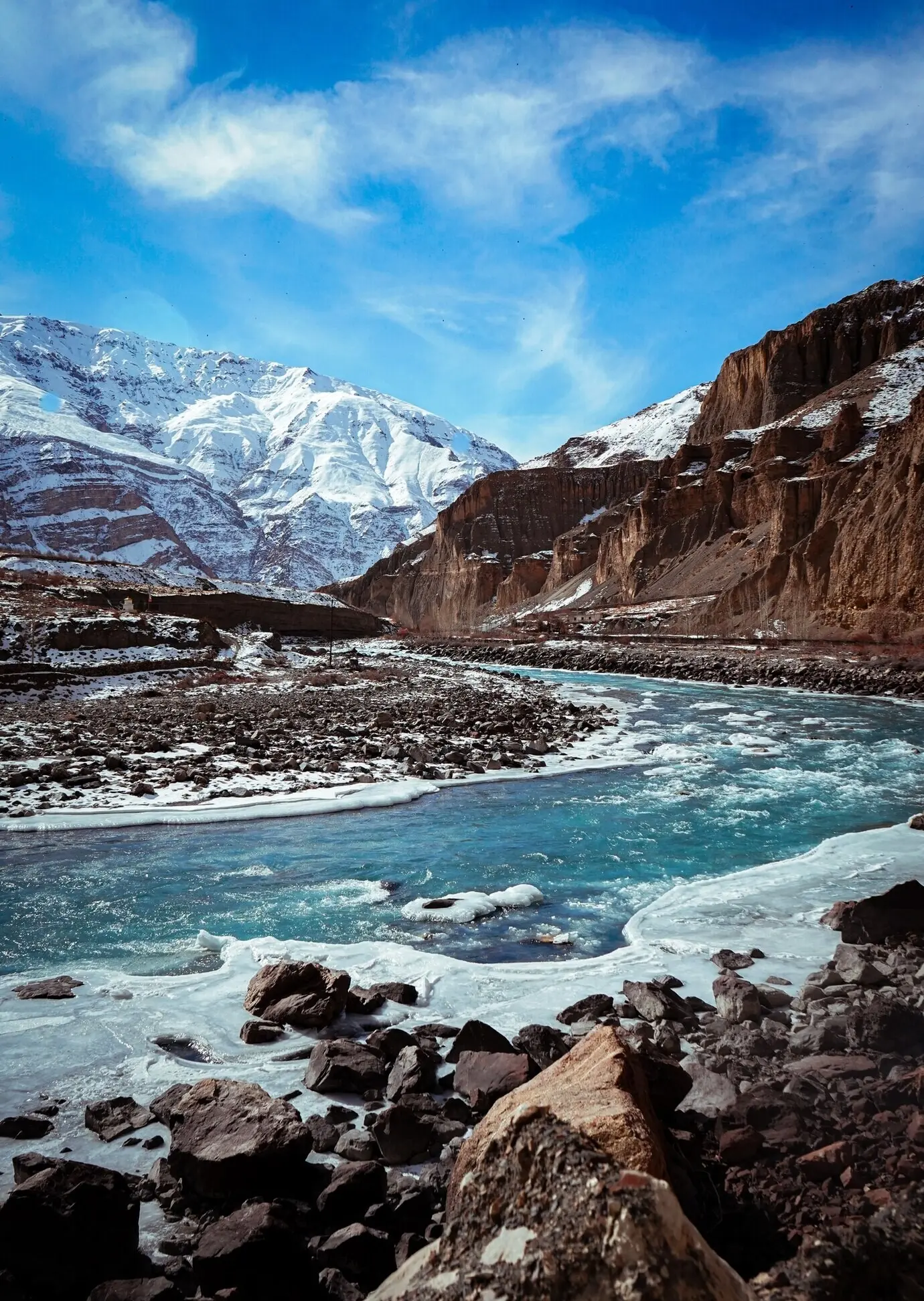 Hochformataufnahme des Spiti-Tals im Winter mit gefrorenem Fluss und schneebedeckten Berggipfeln.